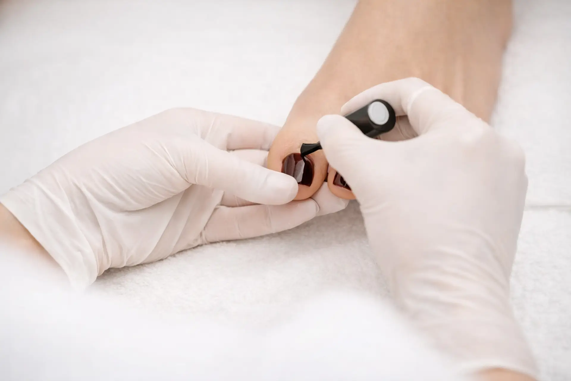 Nail technician applying burgundy polish during a professional pedicure at Aura Day Spa in Thunder Bay.